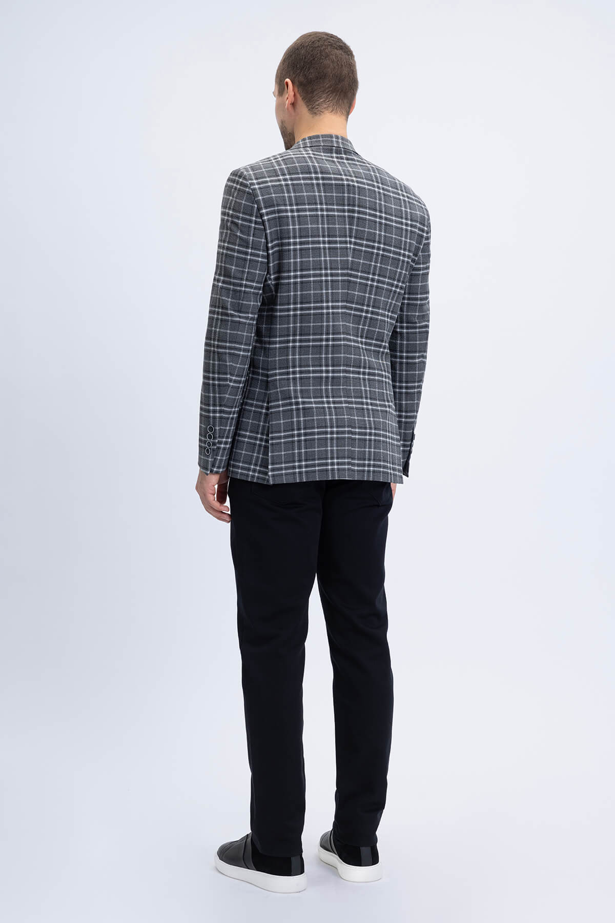 A man wearing a comfort fit notch lapel gray plaid classic blazer with black trousers in dark gray and white tones