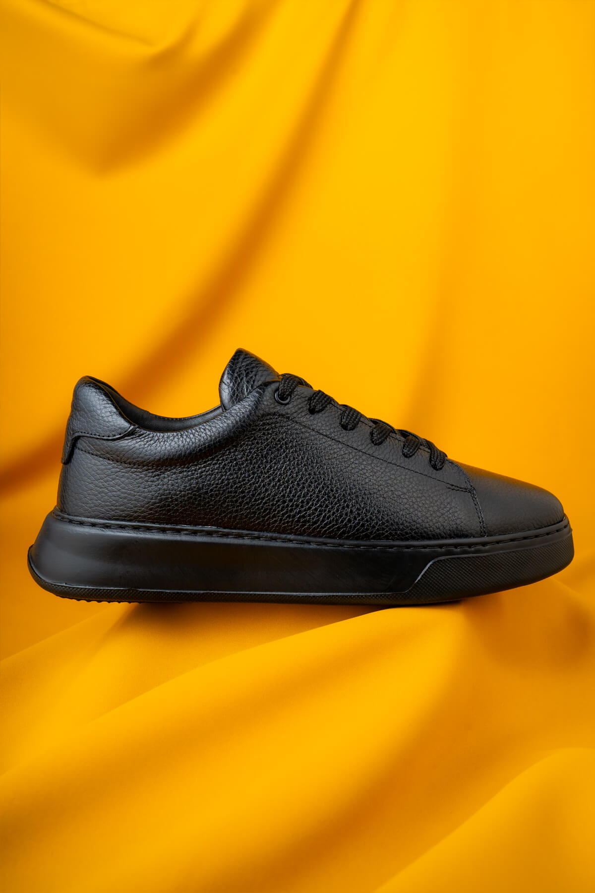 Black leather sneaker with a textured surface and matching laces.