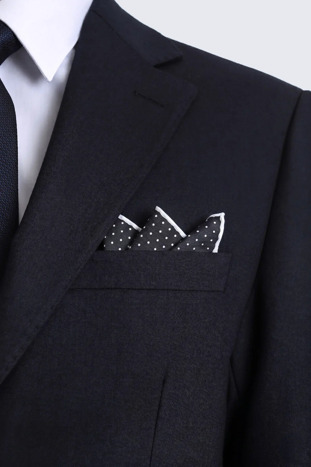 Black polka dot pocket square with white border neatly folded in dark suit breast pocket for smart casual wear