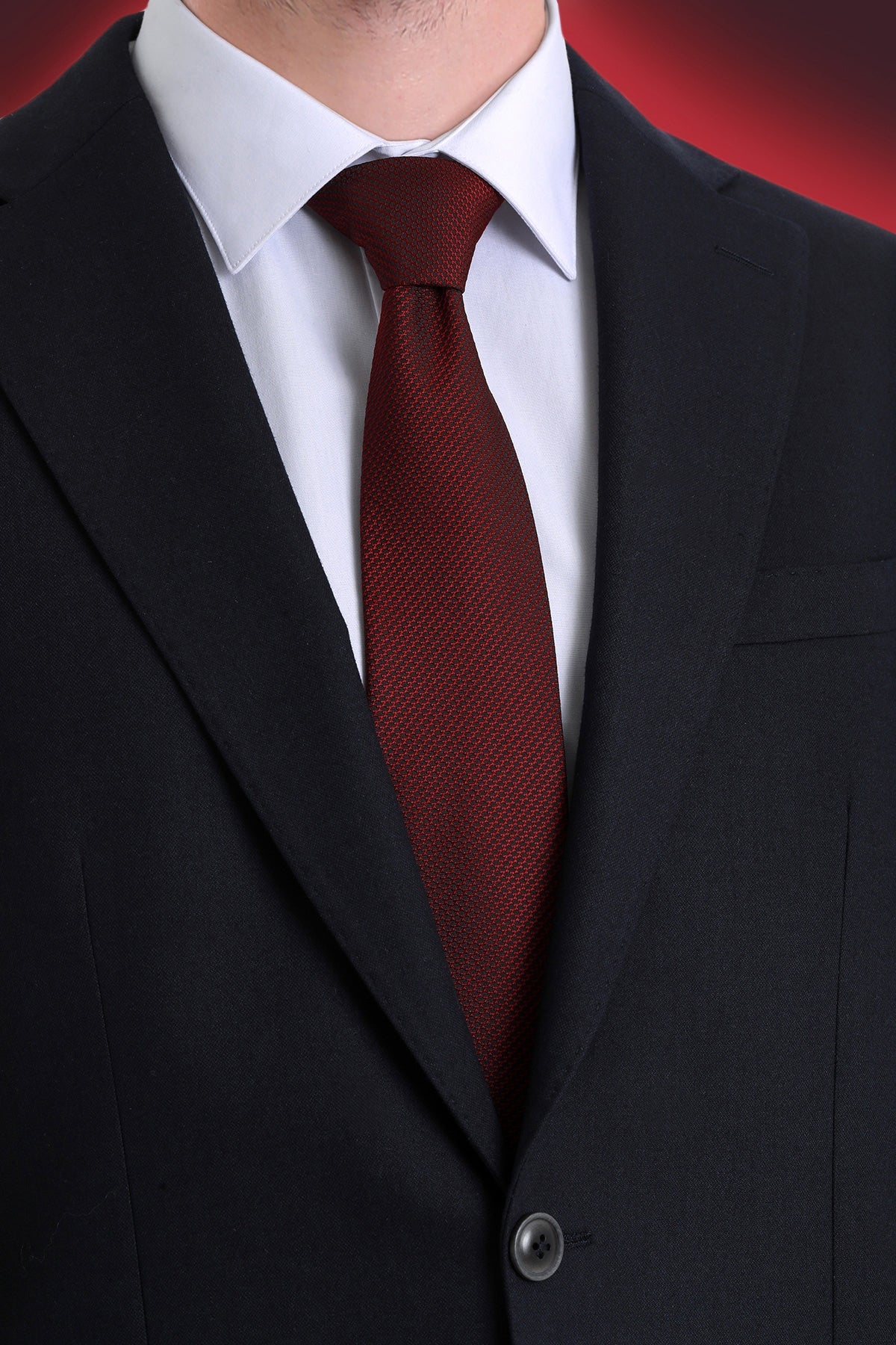 A rich burgundy tie with a subtle textured weave, worn neatly knotted against a crisp white shirt and black suit.