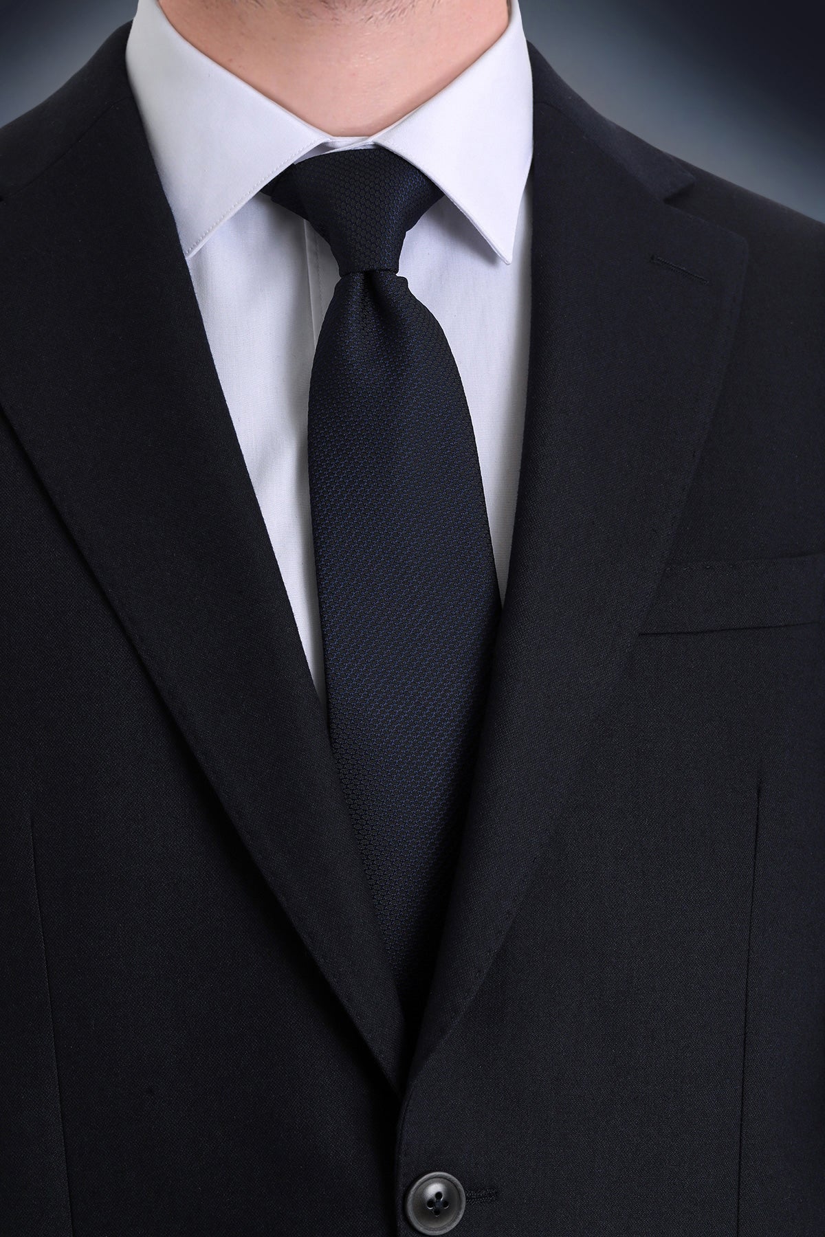 Black silk tie with subtle texture, worn neatly against a white dress shirt and black suit jacket.