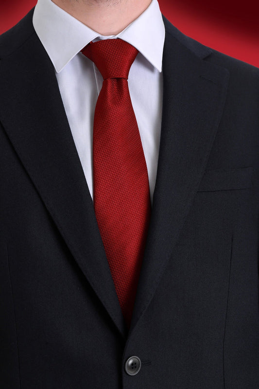 A rich red textured silk tie neatly knotted against a crisp white shirt and black suit.