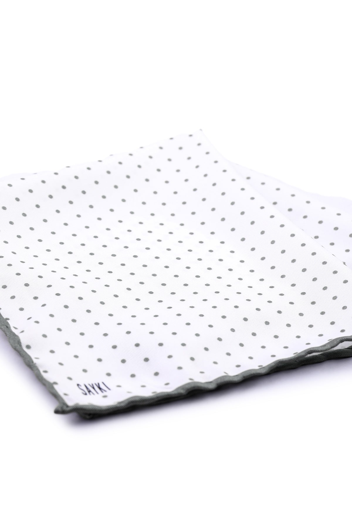 White pocket square with a pattern of small gray polka dots and a scalloped edge, featuring the brand name ’sakki’ embroidered in black at one corner.