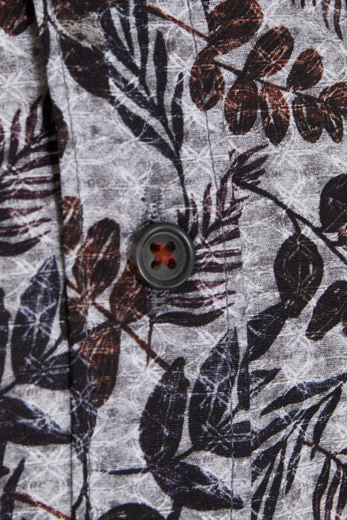 Dark gray button with a red cross-shaped center, set against a fabric featuring black and brown leaf patterns on a light gray background.
