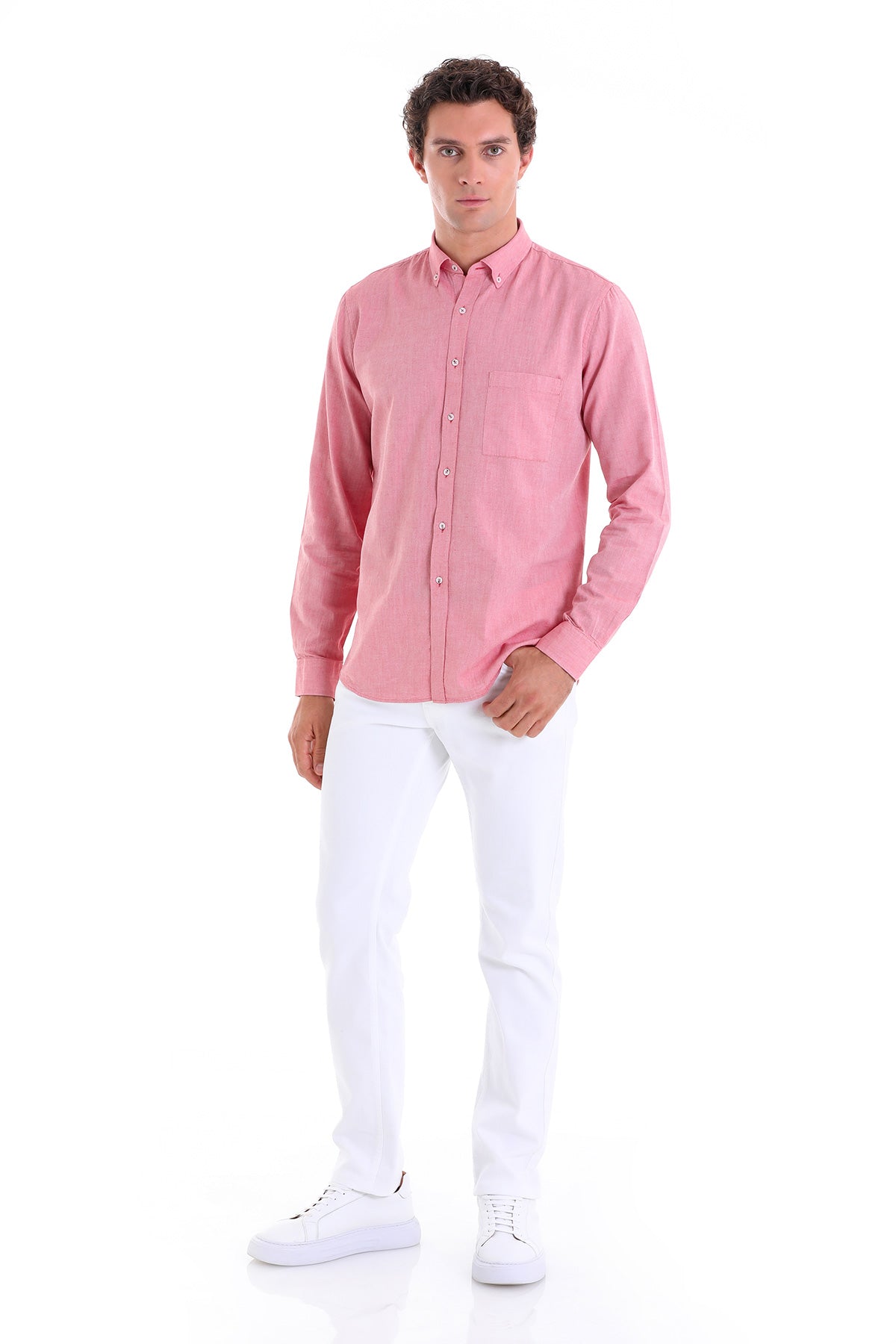 A man wearing a pink long-sleeved button-up shirt with a chest pocket and matching white pants.