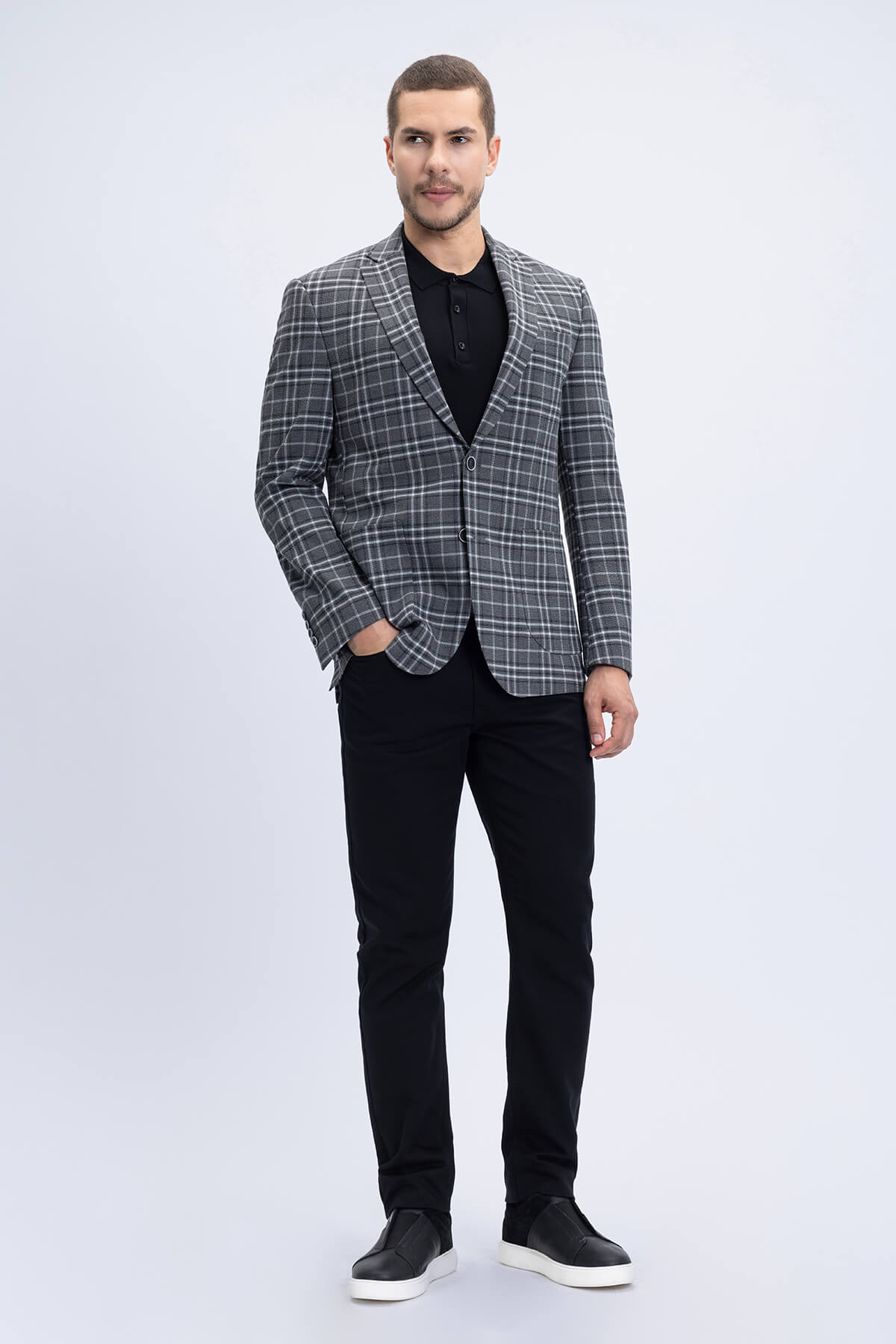A man wearing a comfort fit notch lapel gray plaid classic blazer with black trousers