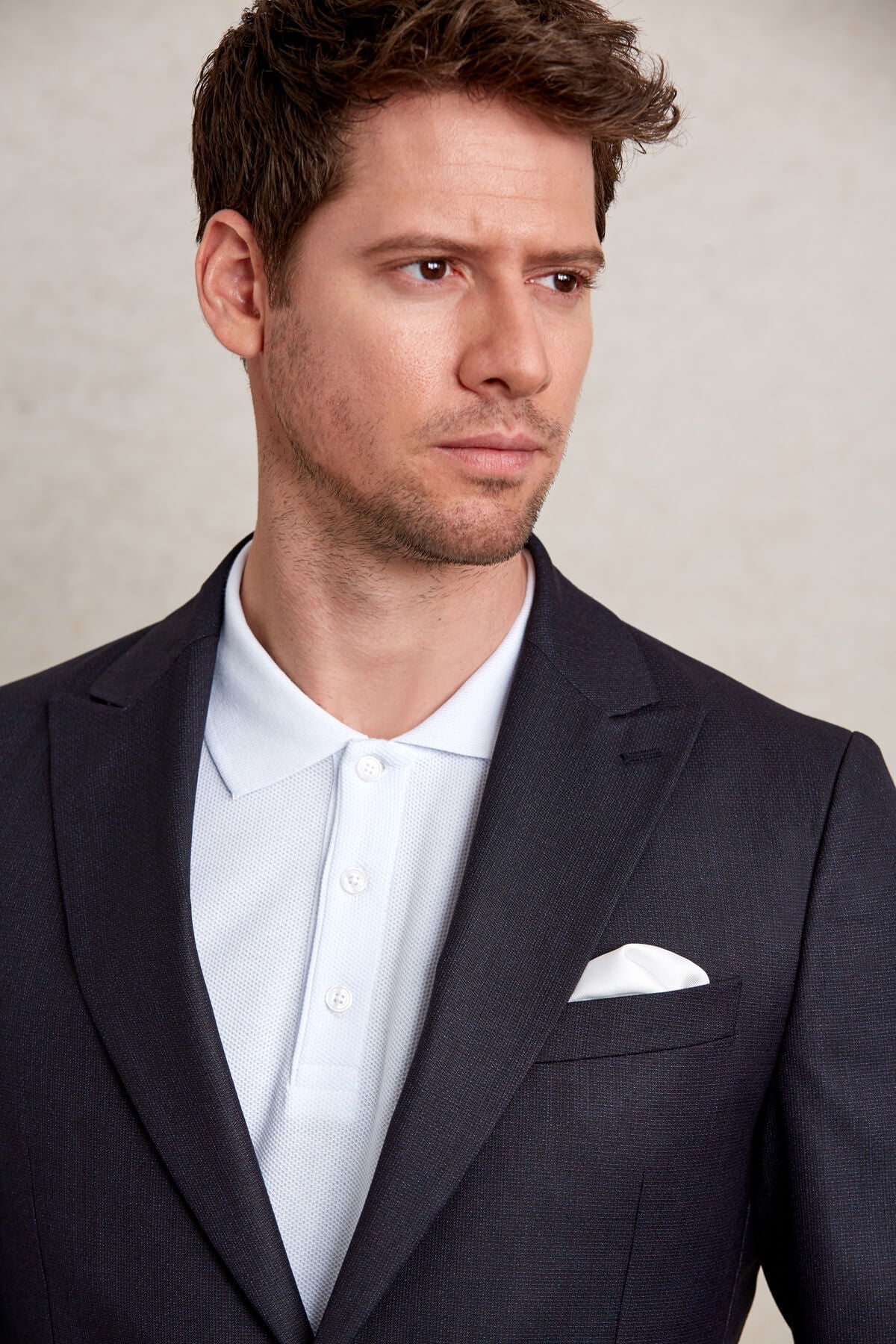 Dark navy textured suit jacket with a crisp white pocket square.