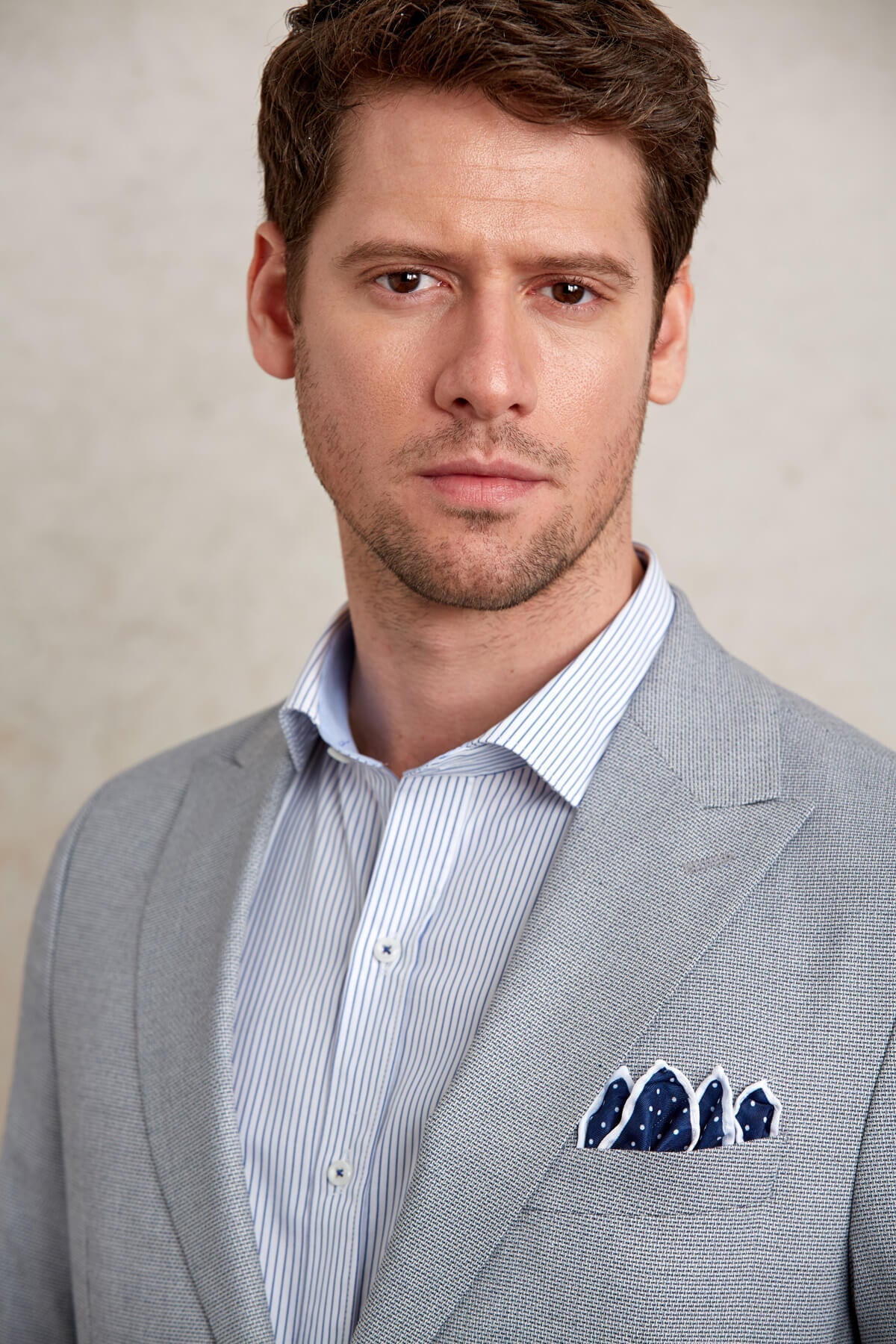 A navy blue pocket square with white polka dots, neatly folded into the breast pocket of a gray textured suit jacket.