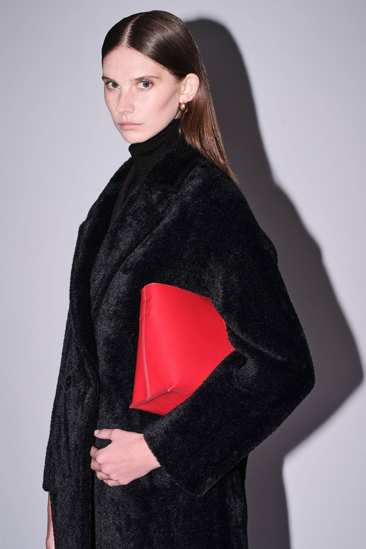 A bold red geometric clutch with a sleek, modern design worn over a black fur coat.