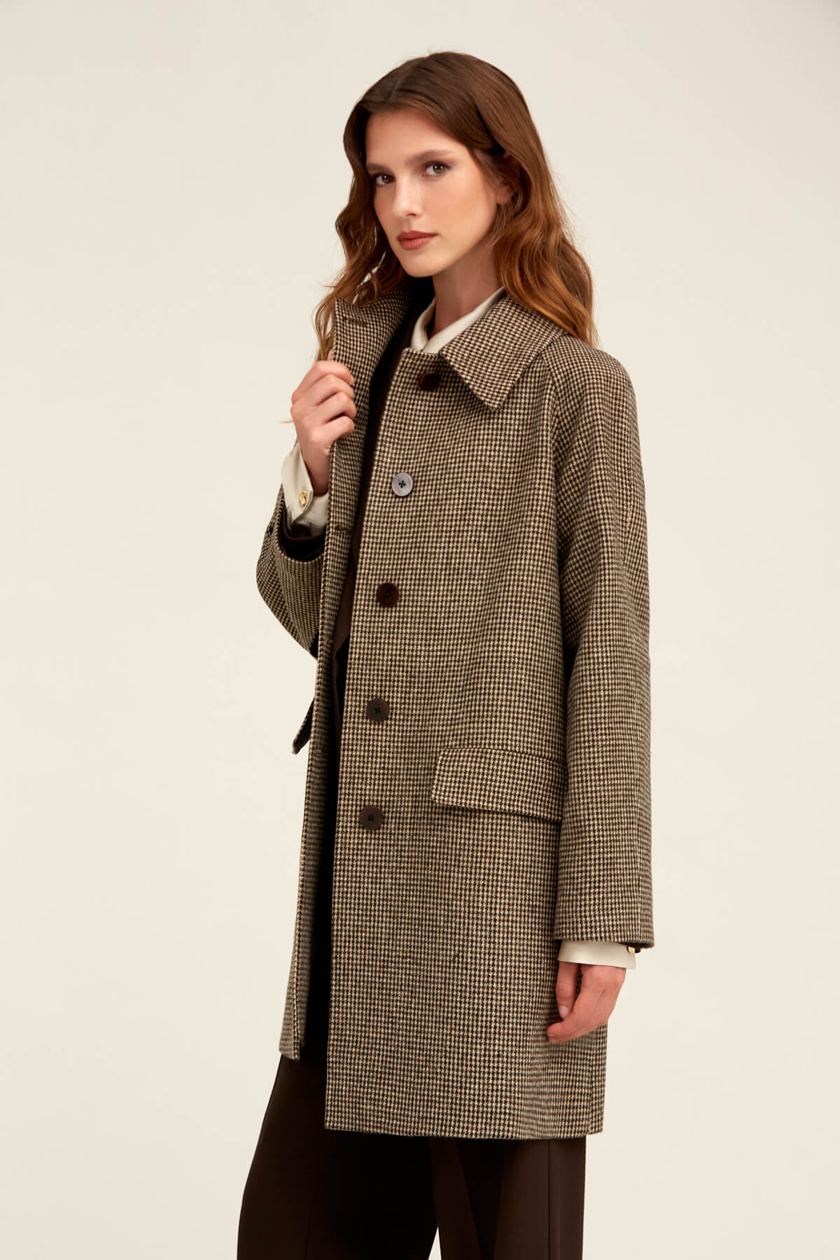 A woman wears a brown and beige houndstooth wool coat with dark buttons.