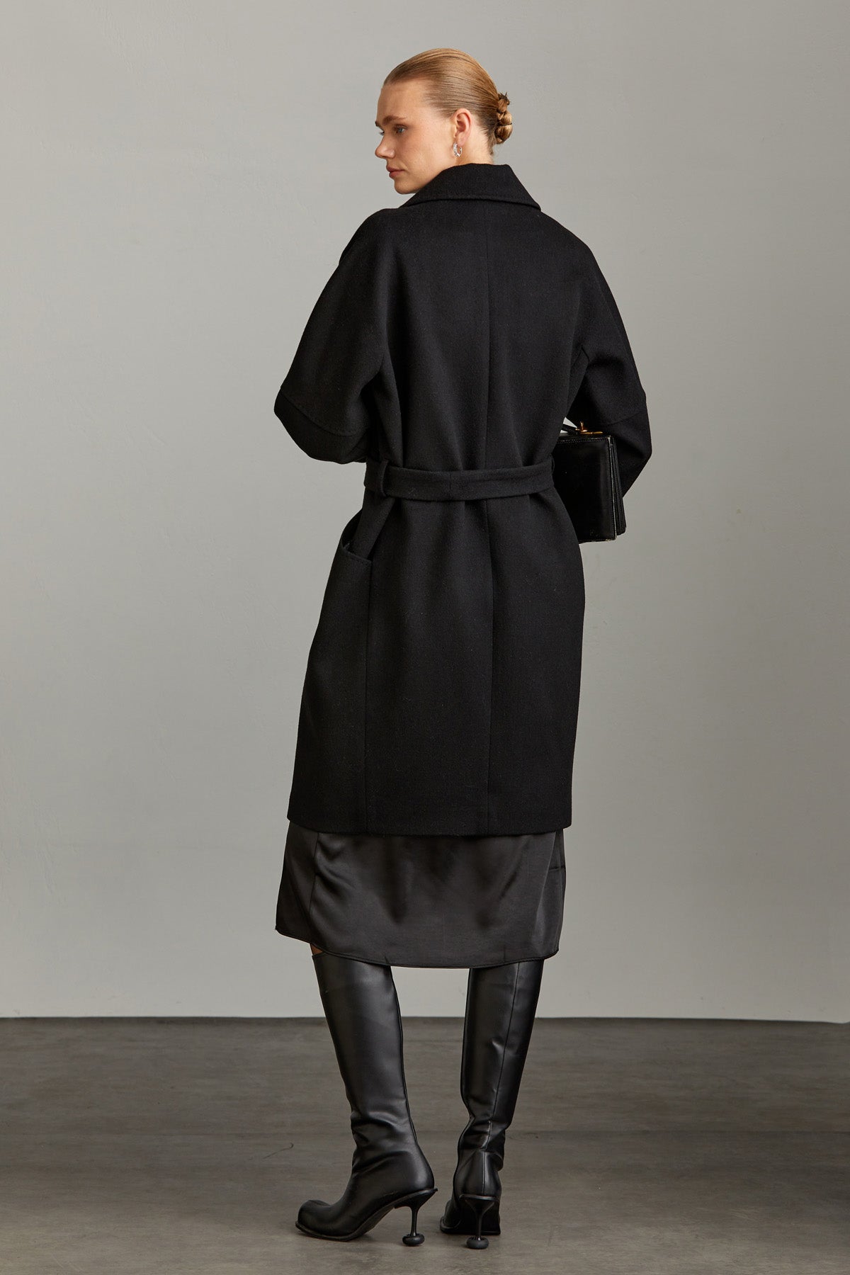 Black wool coat with a belted waist and wide sleeves.