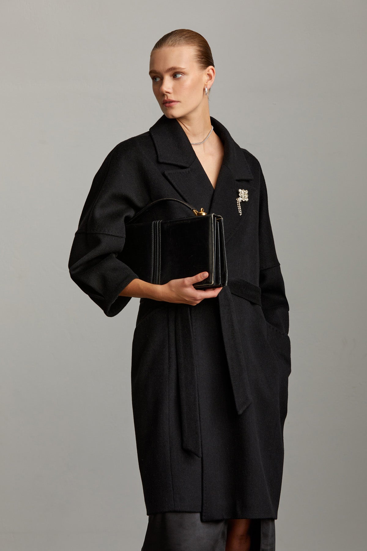 Black velvet box-shaped handbag with gold-tone hardware and a decorative brooch on the front.