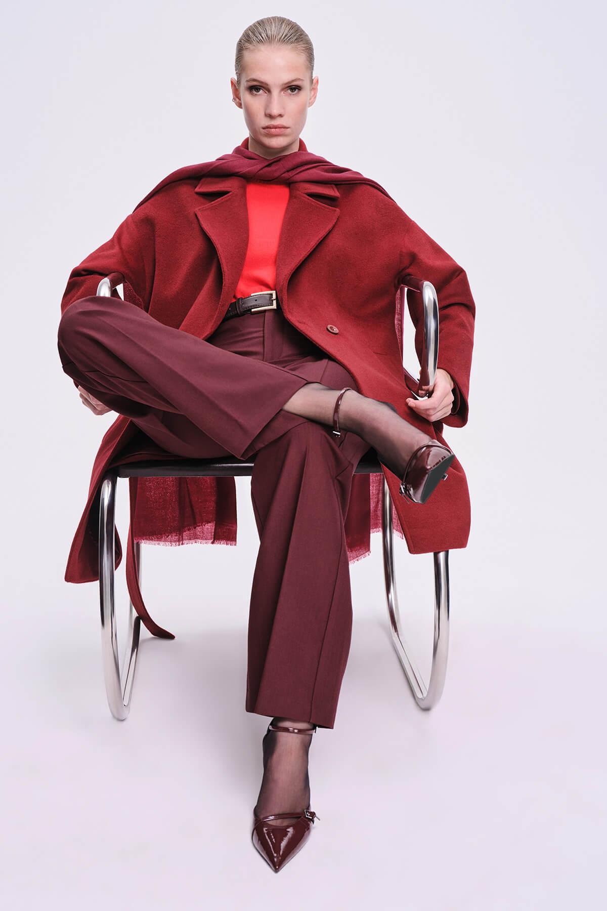 A woman wears a bold red coat with wide lapels and matching burgundy trousers, paired with glossy black heels.