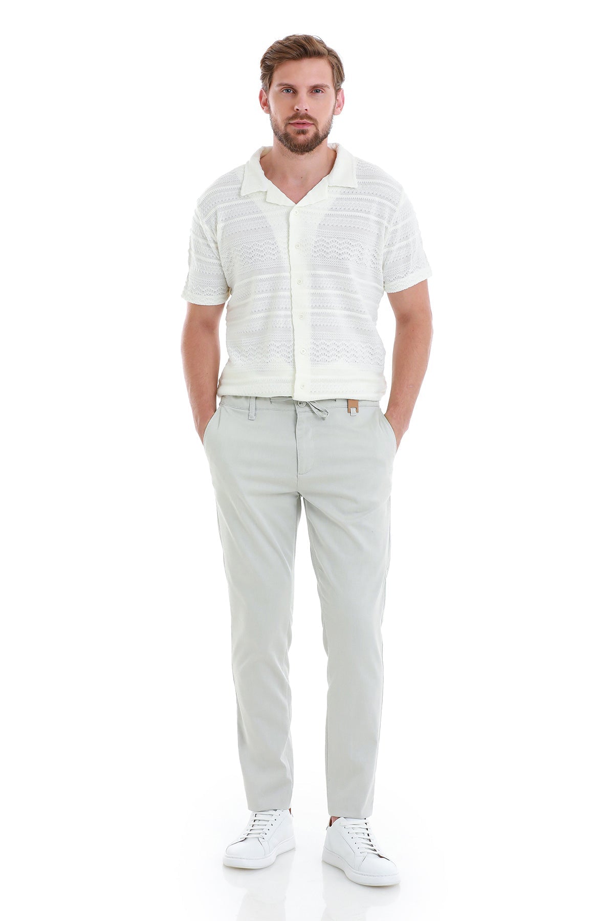 A man wearing a white short-sleeved button-up shirt with subtle horizontal textured stripes and light gray chino pants.