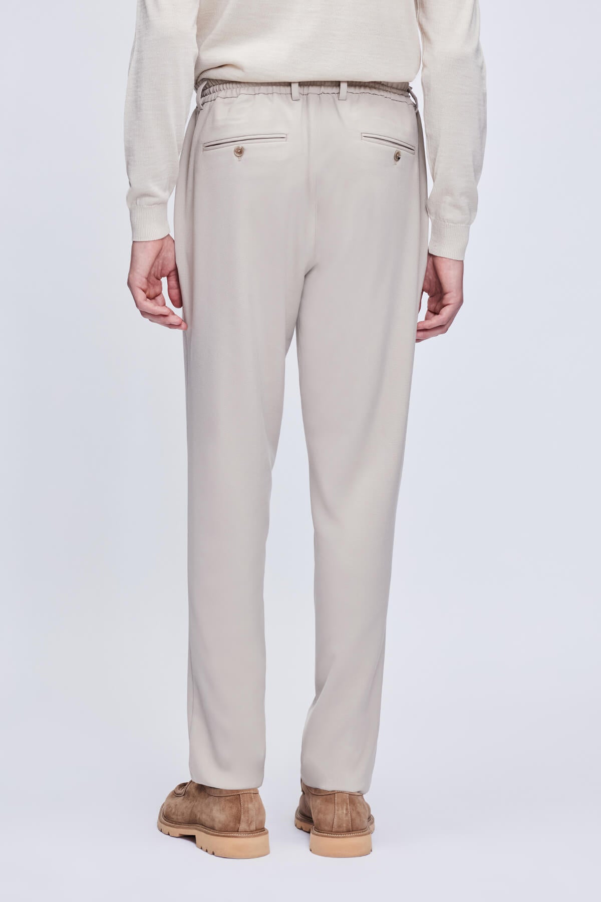 Beige tailored trousers with a drawstring waistband and two front pockets, crafted from smooth, structured fabric.
