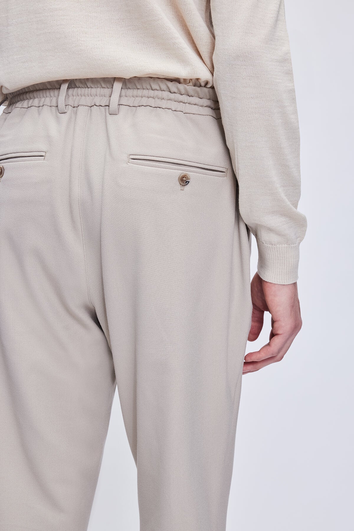 Beige tapered trousers with a drawstring waistband and subtle front pockets featuring metallic buttons.