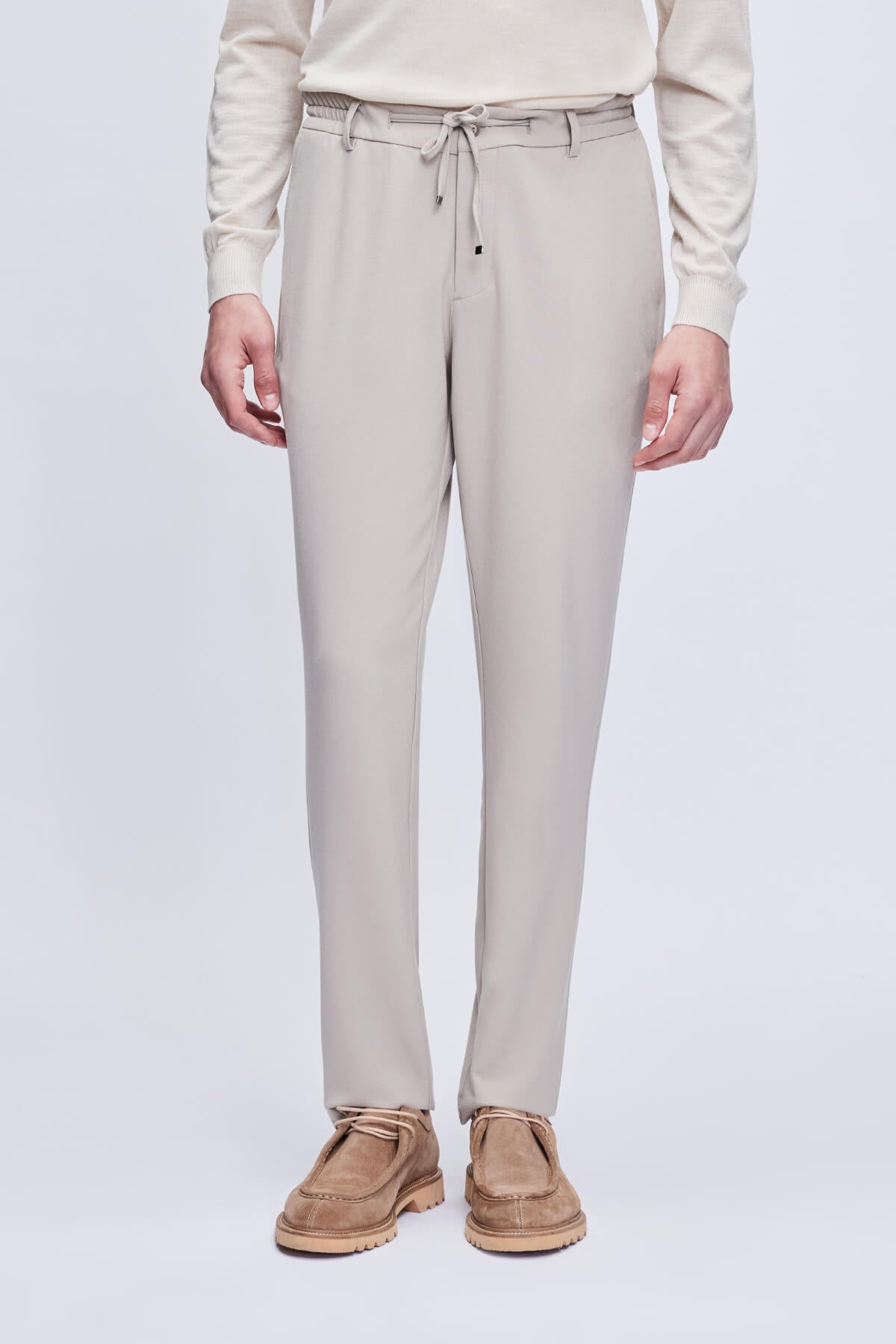 Beige tapered trousers with a drawstring waistband and subtle pleats.