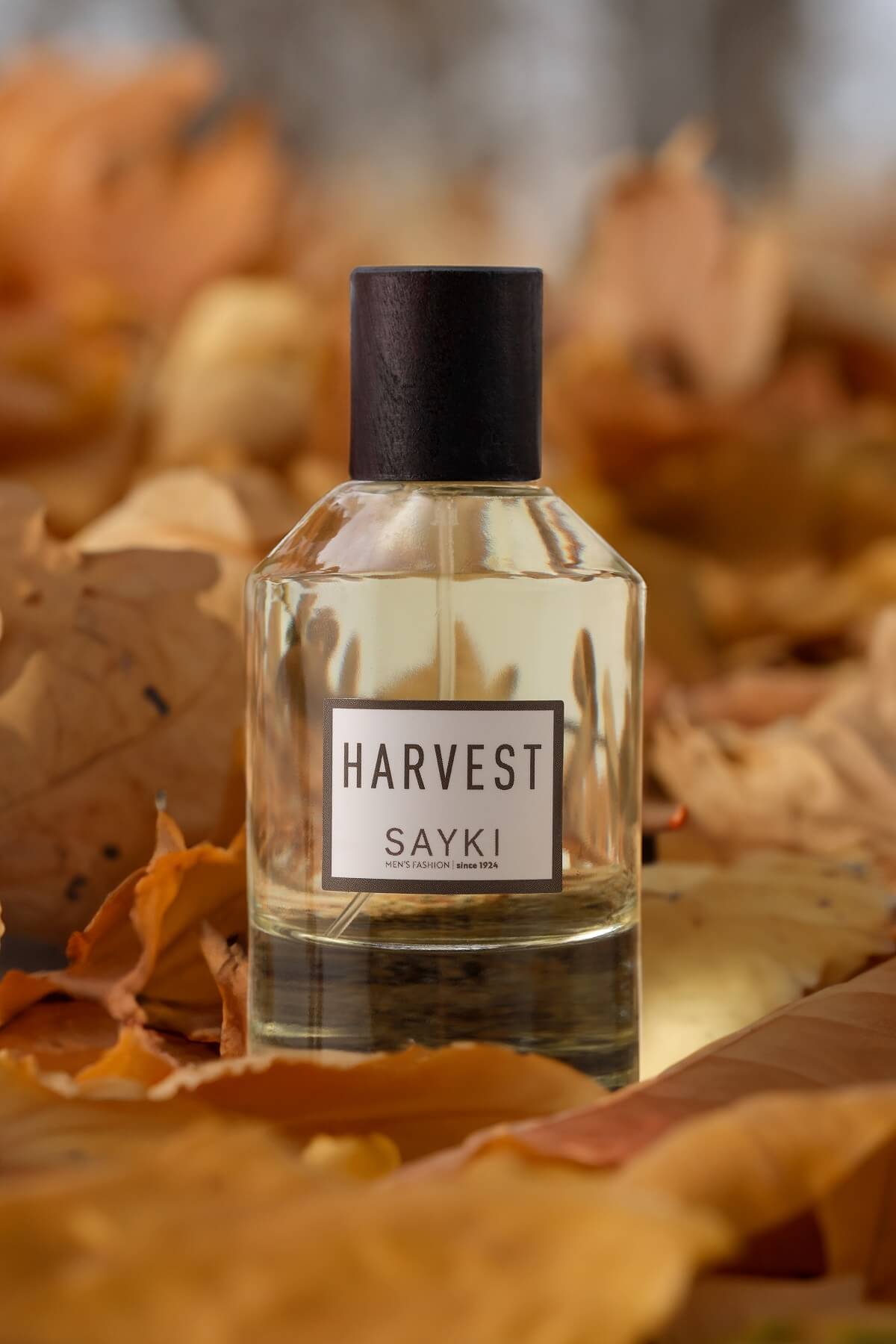 A clear glass bottle of sayki harvest men’s eau de parfum 100 ml with black cap and light amber perfume liquid