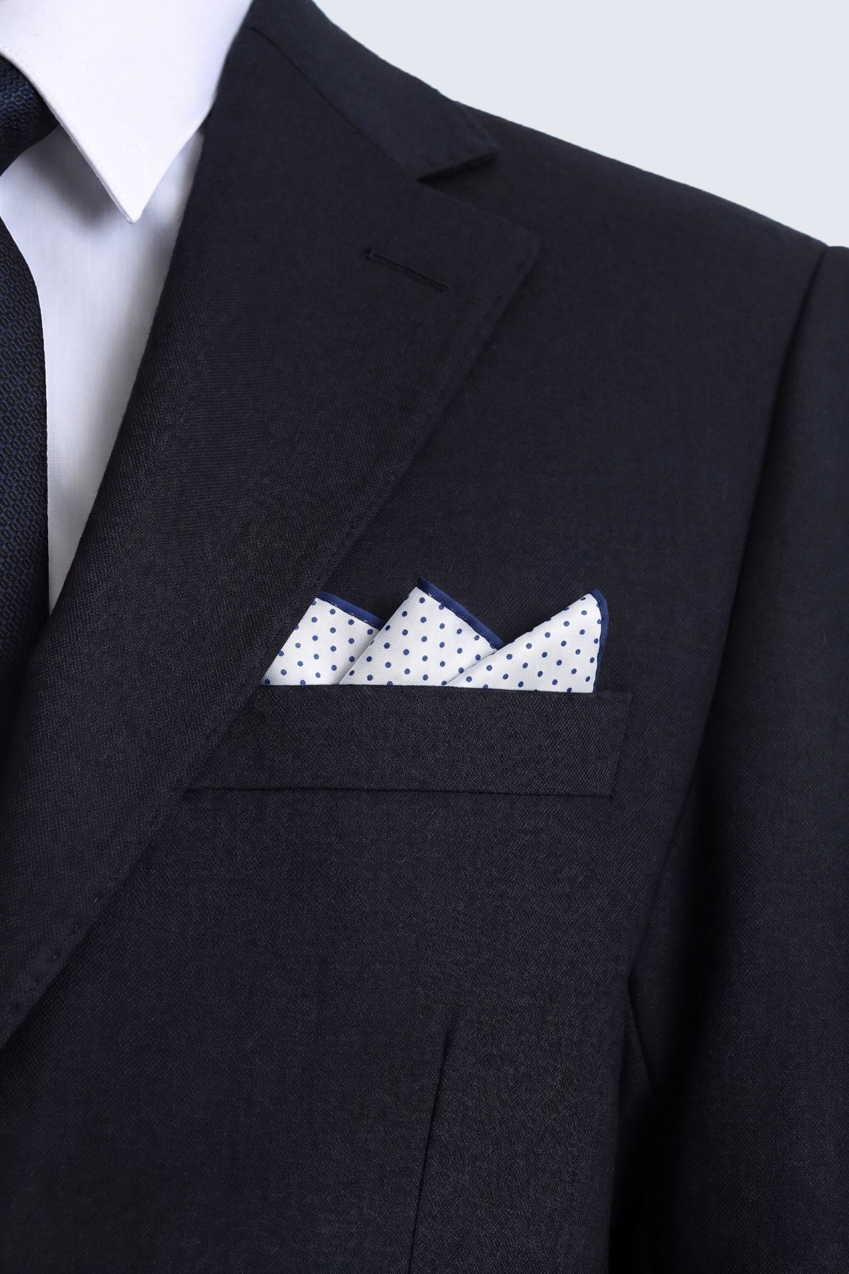 A crisp white pocket square with navy polka dot and light navy polka border folded in a black suit breast pocket