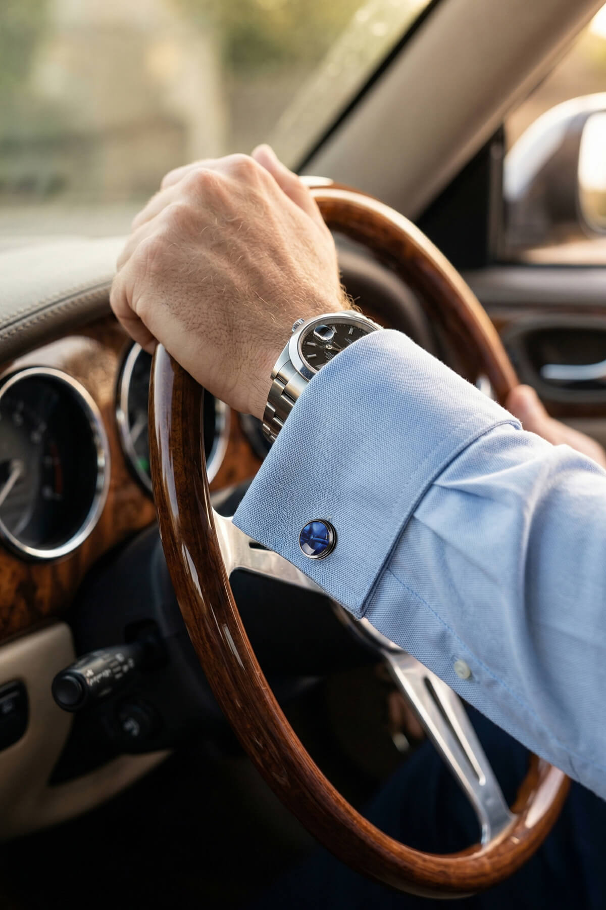 A sleek silver watch with black dial and metallic bracelet worn on wrist beside navy natural stone round cufflinks