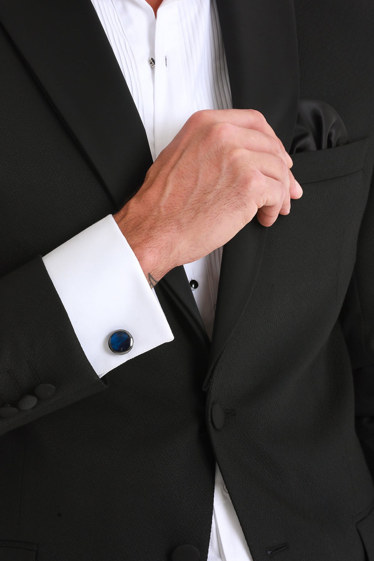 A sleek, round blue cufflink with a polished silver-toned metallic border adorns the white shirt cuff.