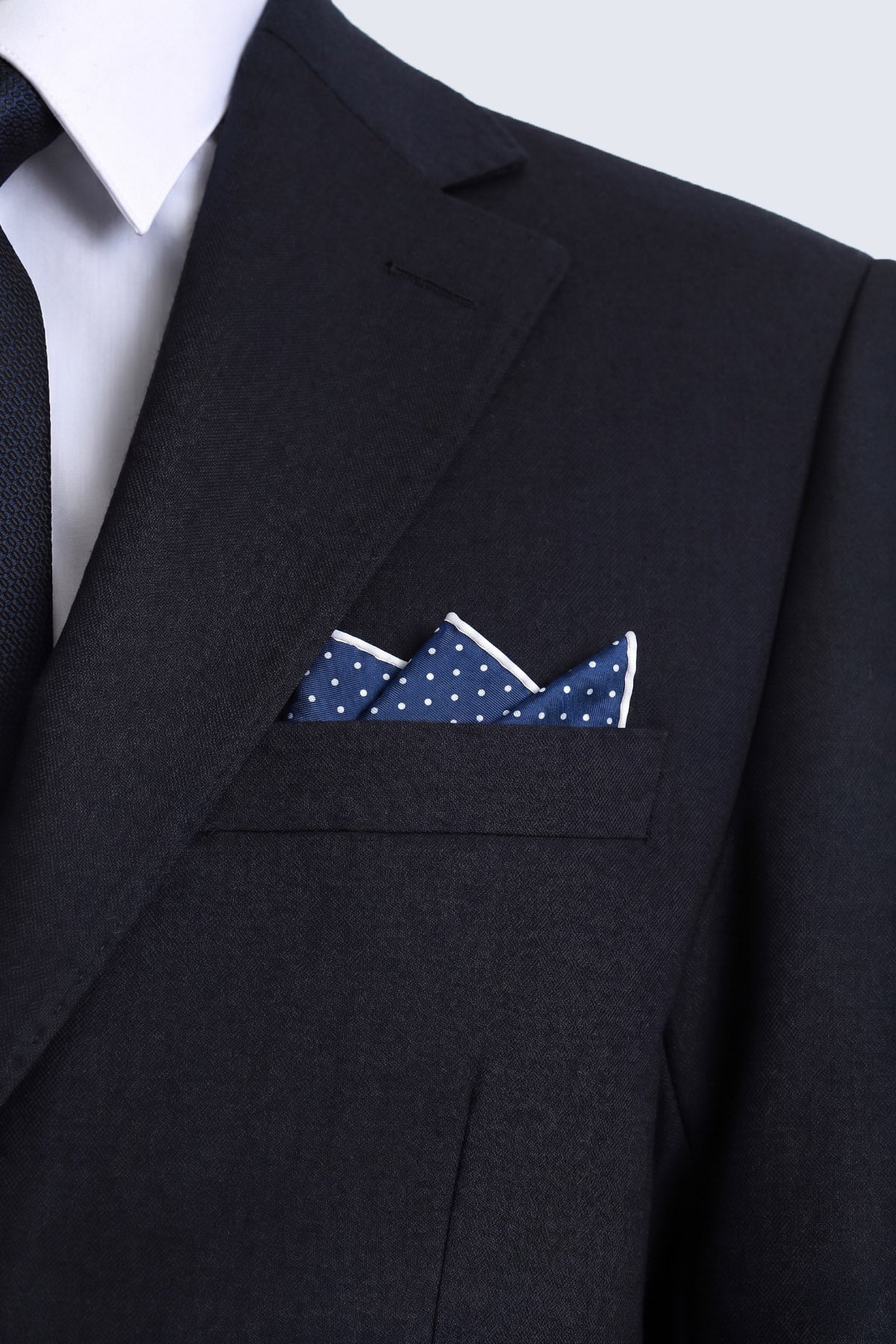 Navy polka dot pocket square with white polka dots and crisp white border folded in black suit jacket pocket