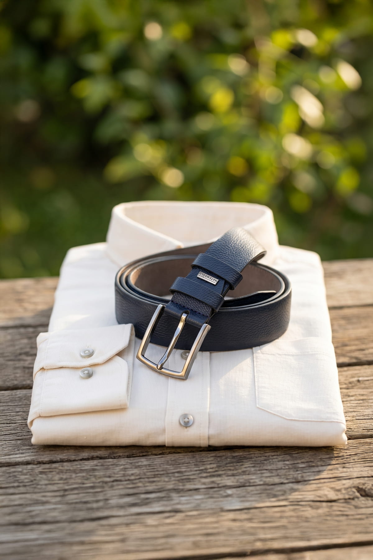 Navy sport faux leather belt in navy with gold-toned buckle resting on folded white dress shirt for smart casual wear