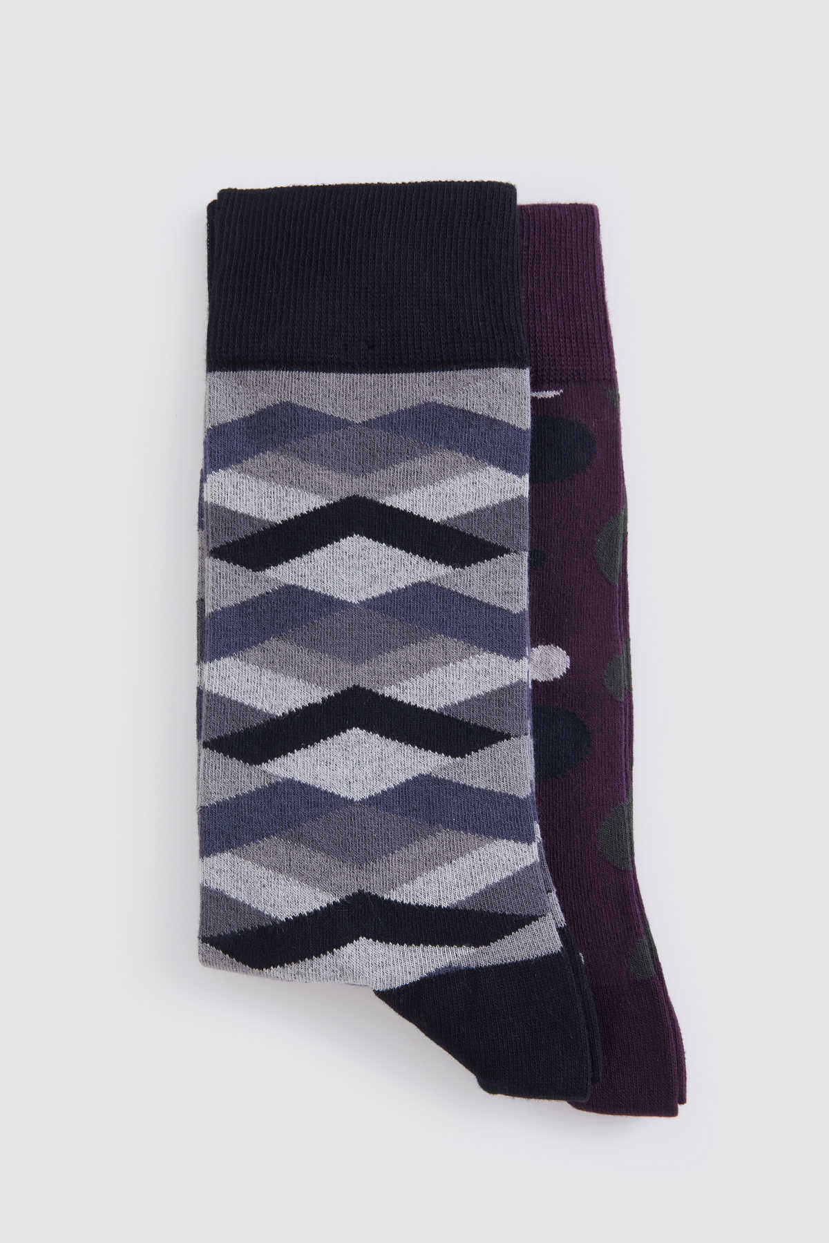 A pair of patterned socks, one featuring a geometric chevron design in shades of gray and black with a solid black cuff and toe, the other displaying dark purple fabric adorned with green polka dots.