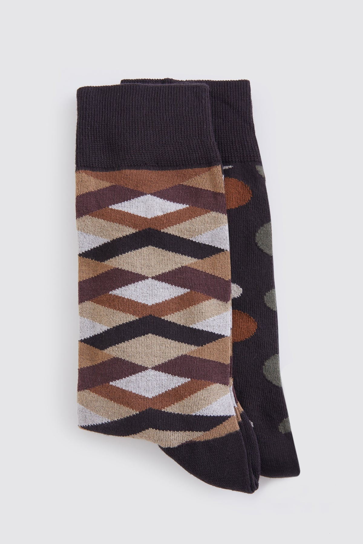 A pair of patterned socks featuring a geometric design in earthy tones and black, with one sock displaying an argyle-like motif and the other showcasing camouflage-style dots.