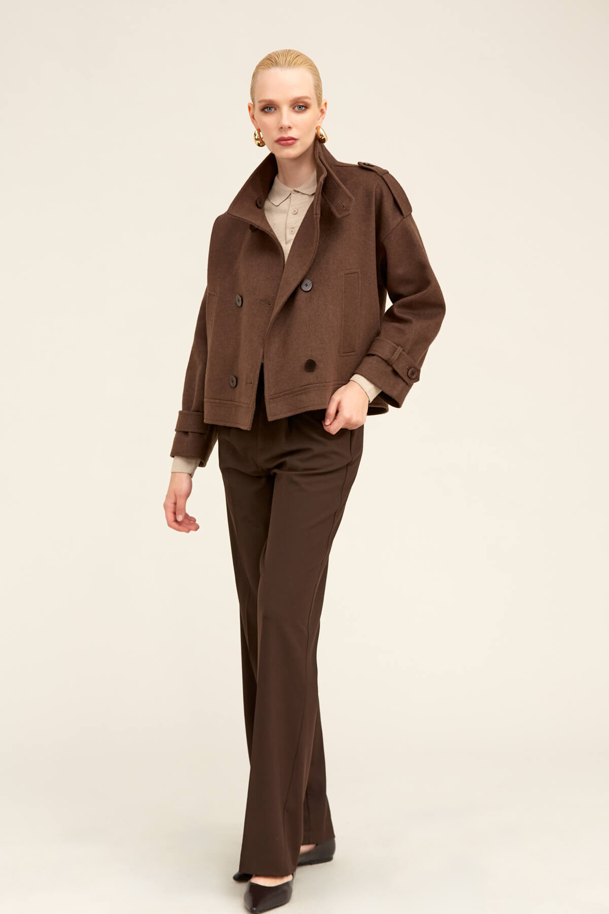 Brown double-breasted trench coat with structured shoulders and flap pockets.