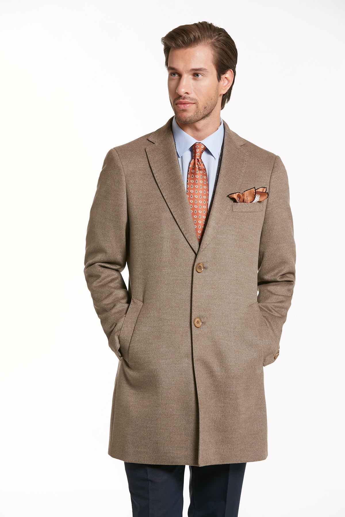 A tailored beige overcoat with a subtle textured weave, featuring three matching buttons and a neatly folded pocket square in coordinating orange-toned fabric.