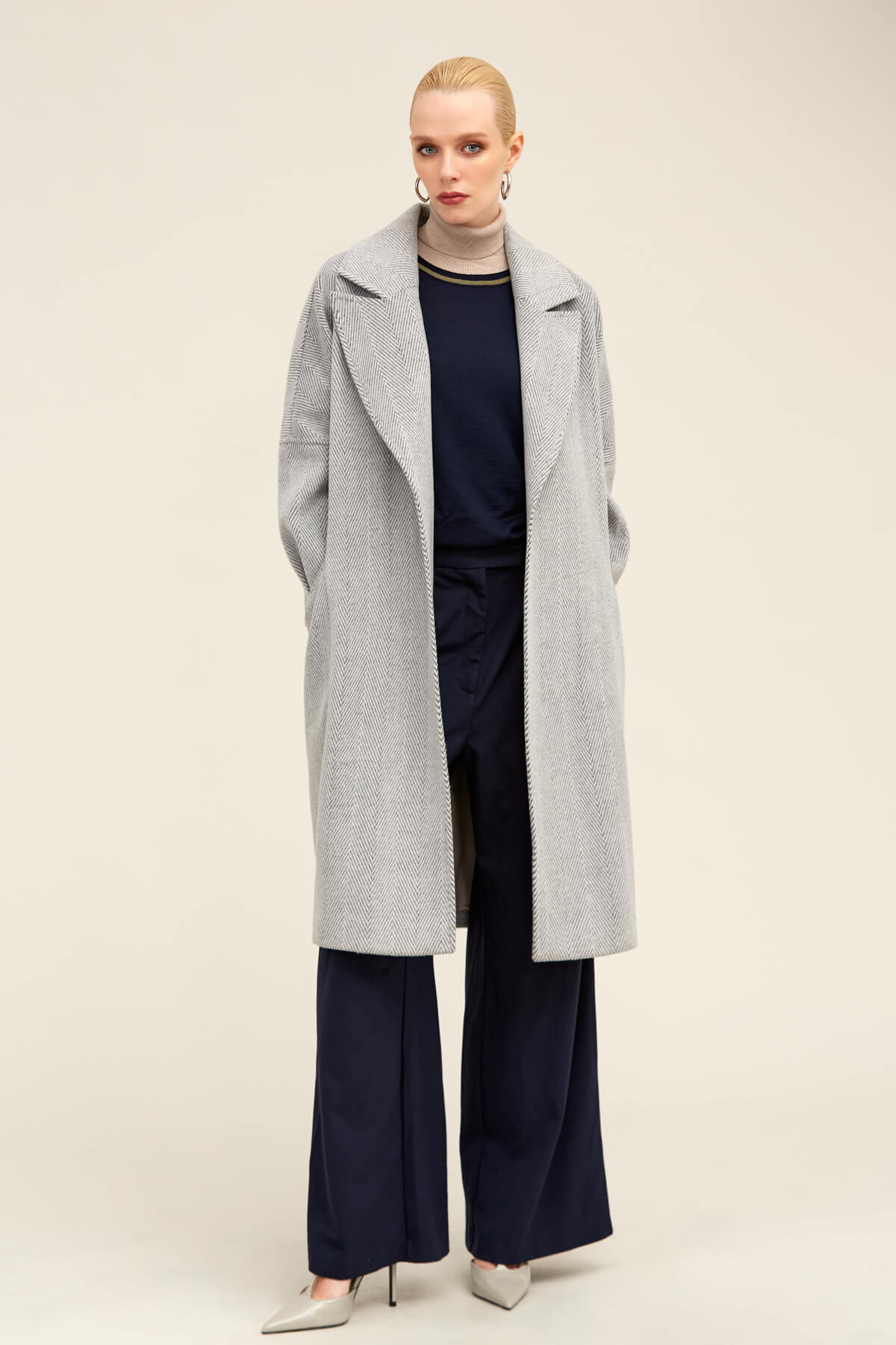 A long, light gray herringbone wool coat with a classic collar and wide sleeves.
