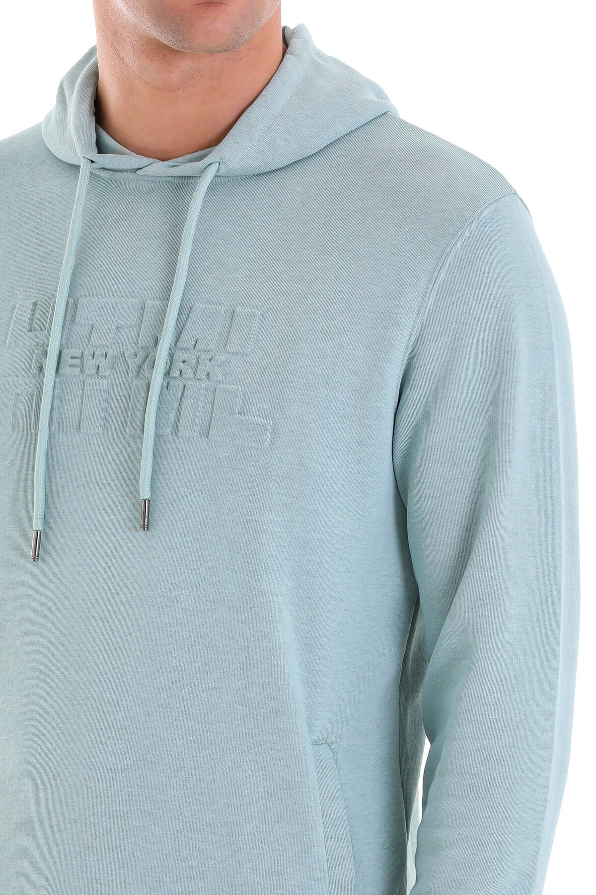 Light blue hoodie with a subtle textured fabric, featuring an embossed ’new york’ logo across the chest and matching drawstrings ending in metallic aglets.