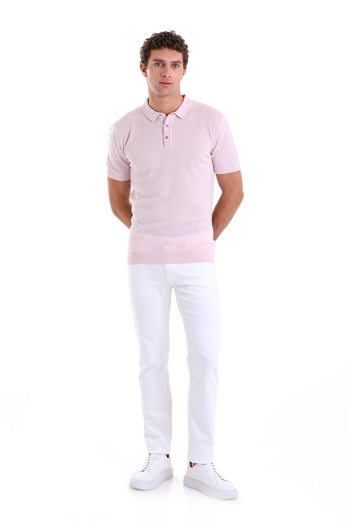 A man wearing a light pink short-sleeved polo shirt with a subtle textured pattern and white pants.