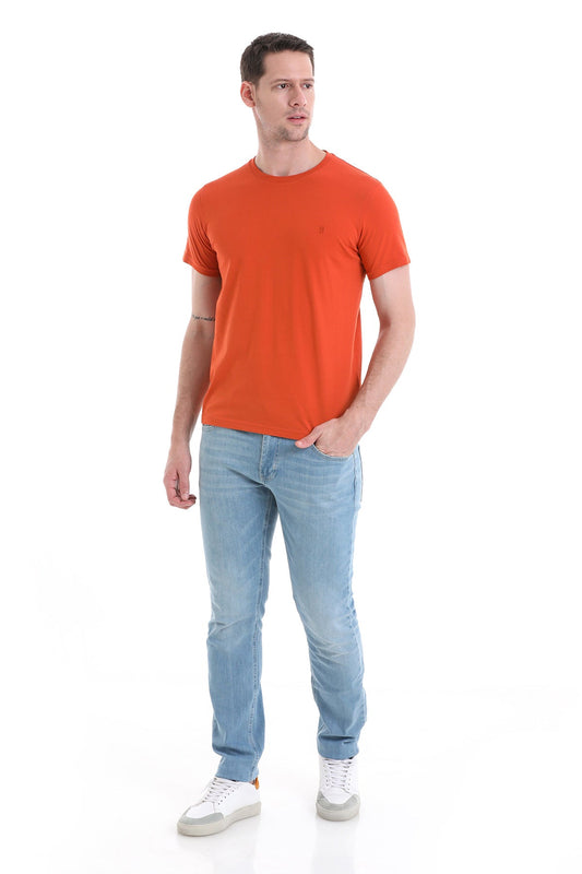 A man wearing a vibrant orange short-sleeved t-shirt with a small embroidered logo on the chest, paired with light blue denim jeans and white sneakers.