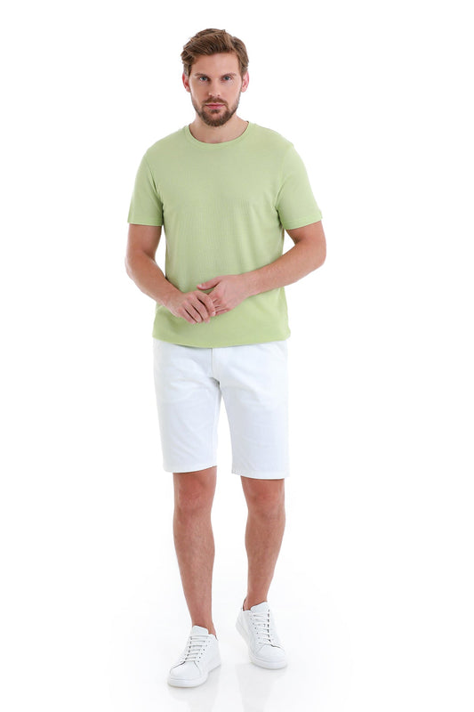 A man wearing a light green, short-sleeved crew neck t-shirt paired with white shorts and white sneakers.