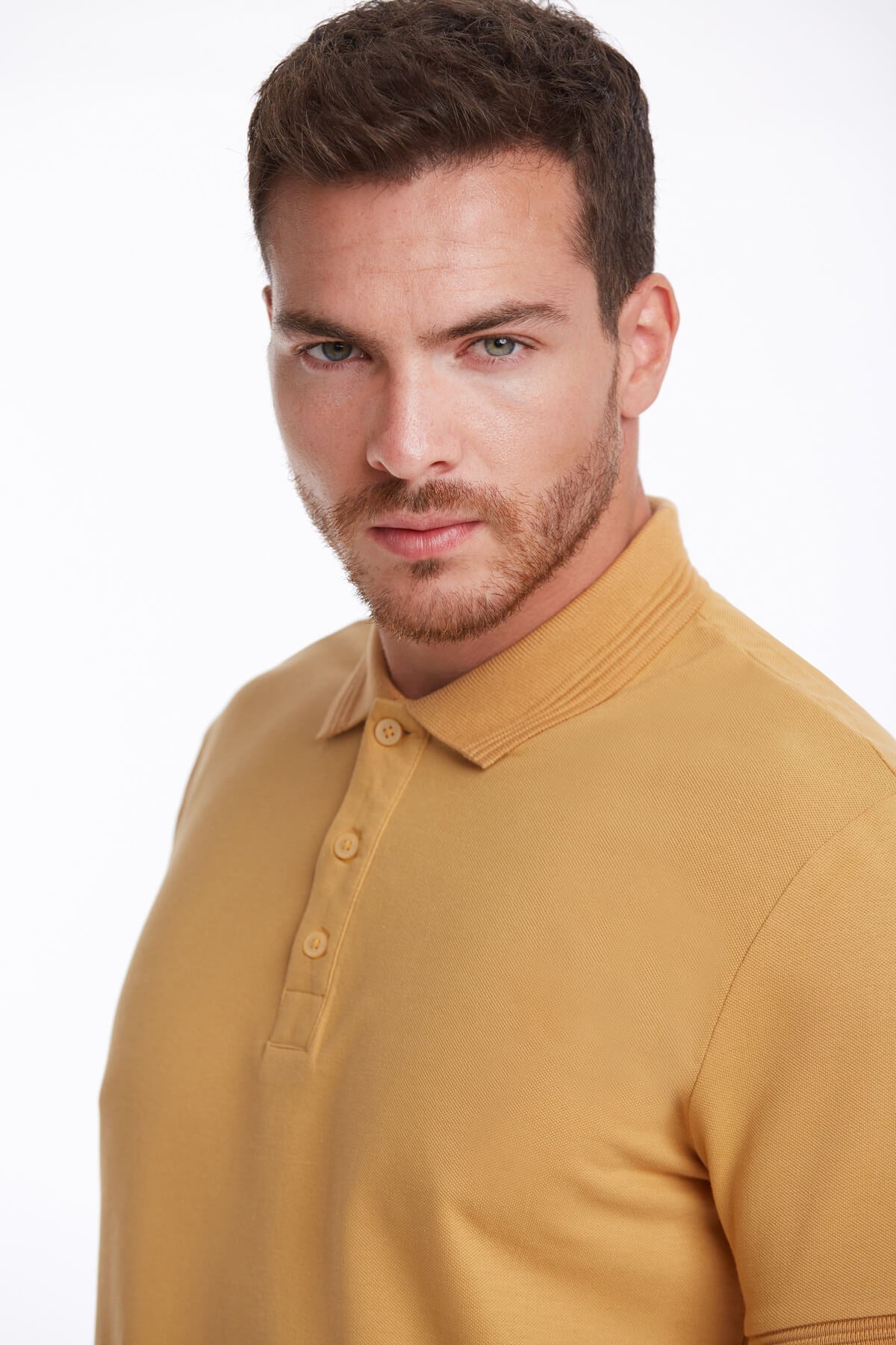 A man wearing a mustard-yellow, short-sleeved polo shirt with a ribbed collar and buttoned placket.