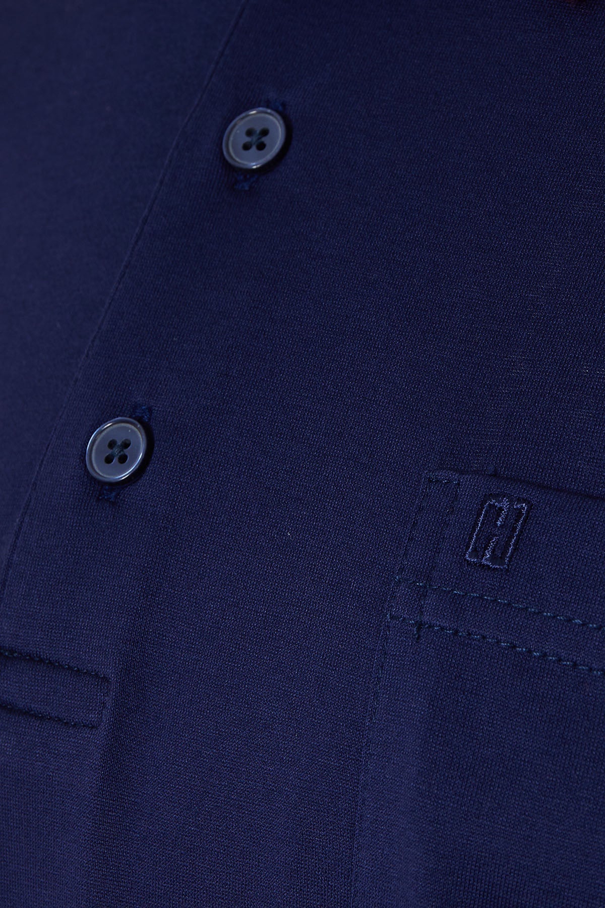 Dark blue textured fabric shirt with black four-hole buttons and a subtle embroidered logo on the chest pocket.