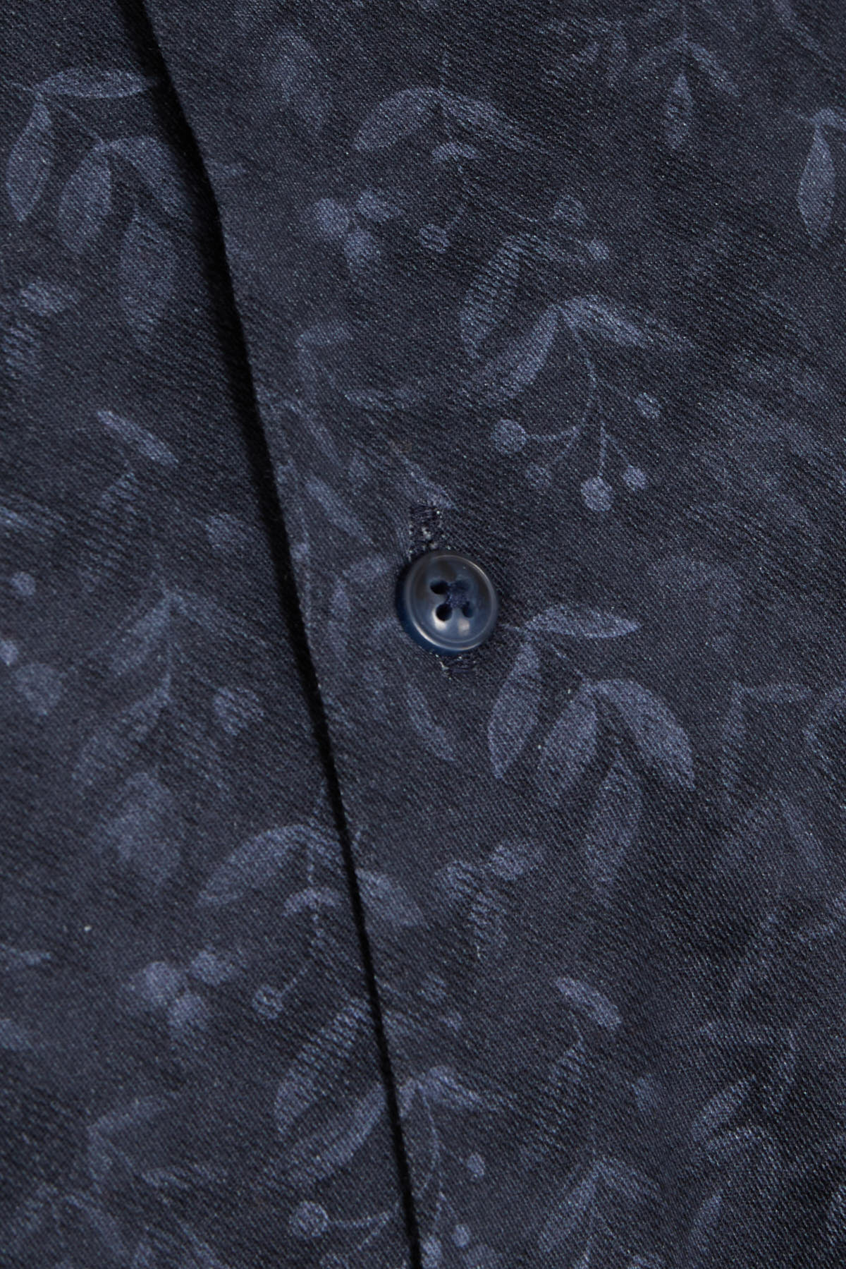 Dark blue button with a subtle sheen, set against fabric featuring an intricate leaf pattern in matching tones.