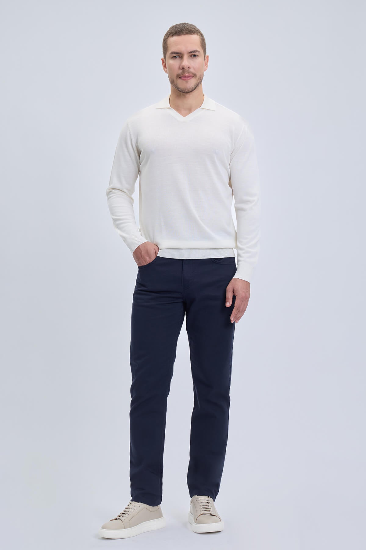 A man wearing a regular fit wool blend white johnny polo sweater with ribbed cuffs and dark navy trousers