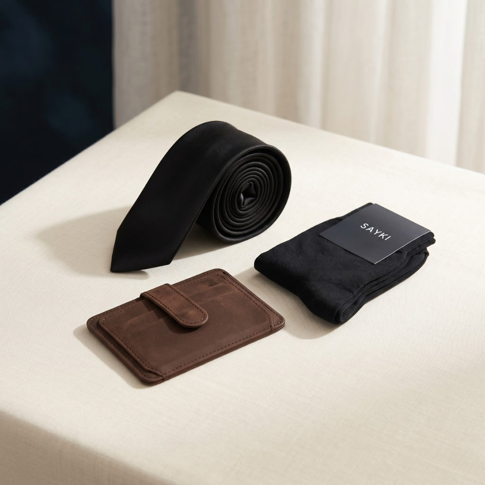 Black tie, brown wallet, and black socks with 'SAYKI' packaging on a white surface.