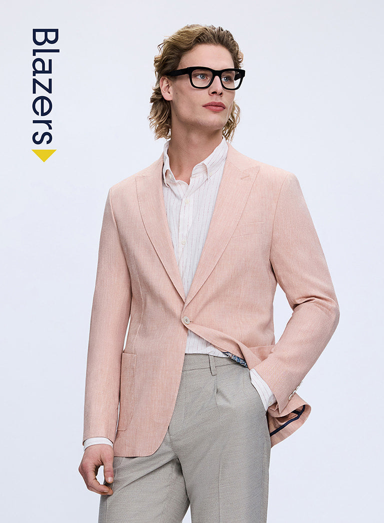 Man wearing a light pink blazer over a white shirt with gray pants on a light gray background.