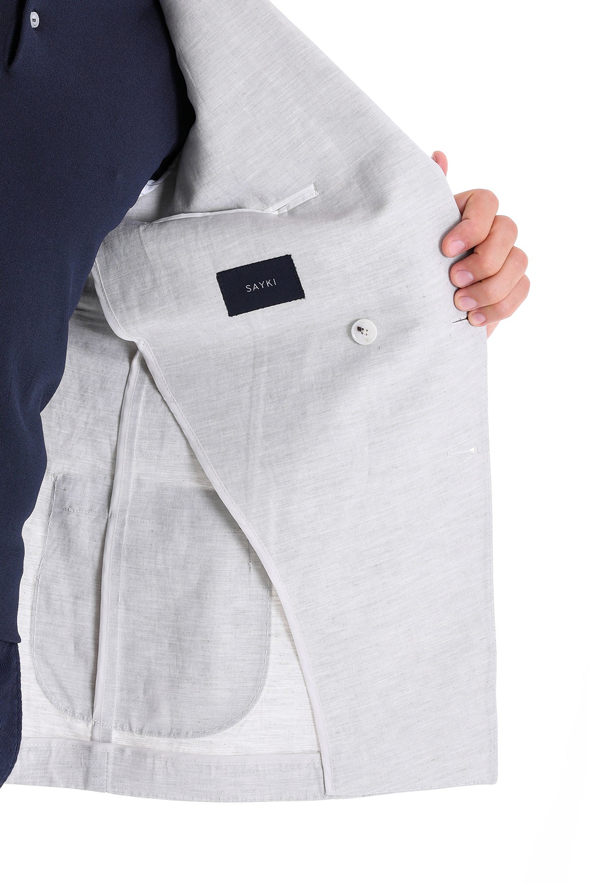 Light gray linen blazer with a subtle texture and a black brand label reading ’sayki’ on the inner pocket.