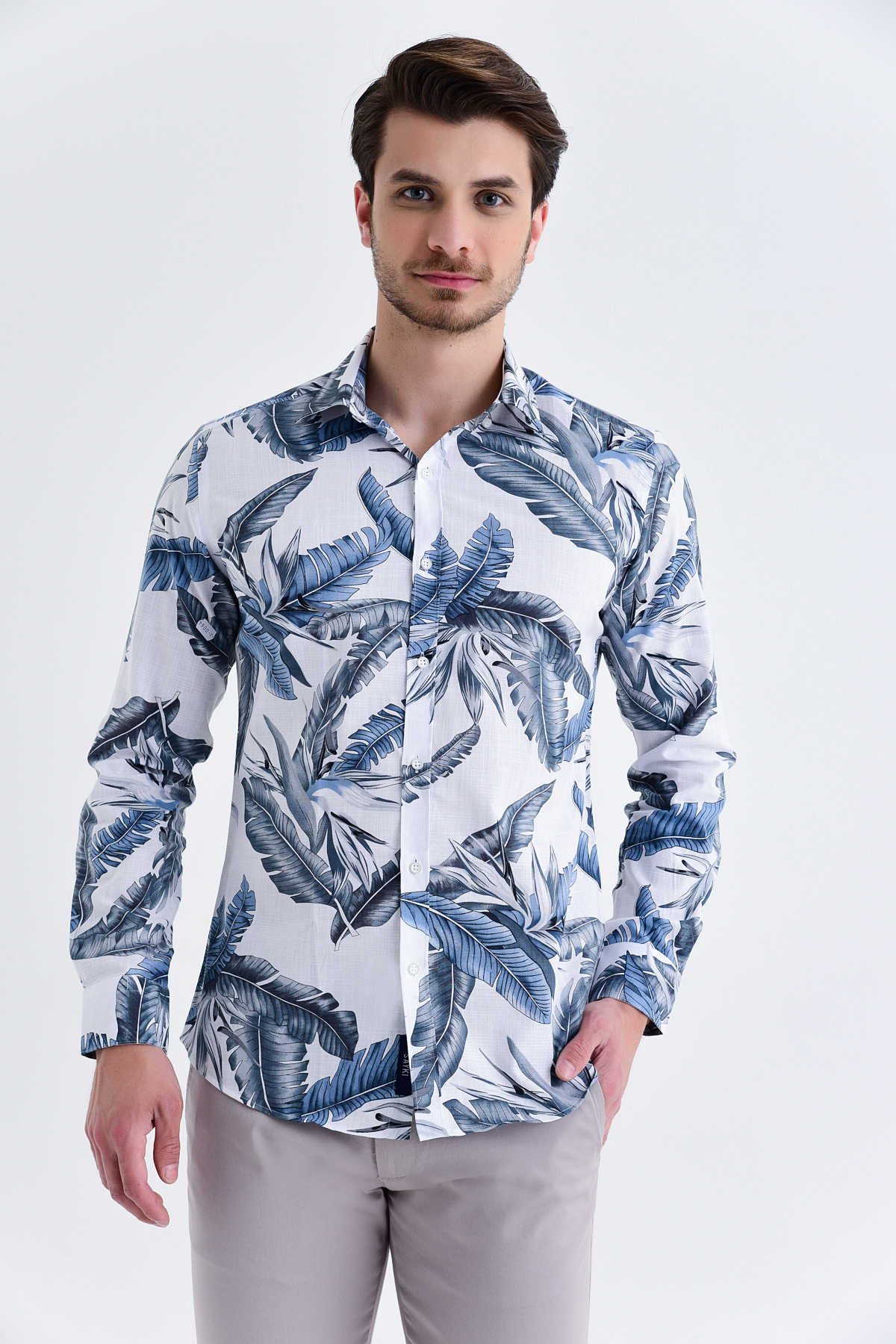A man wearing a white long-sleeved button-up shirt with a bold blue and gray tropical leaf pattern.