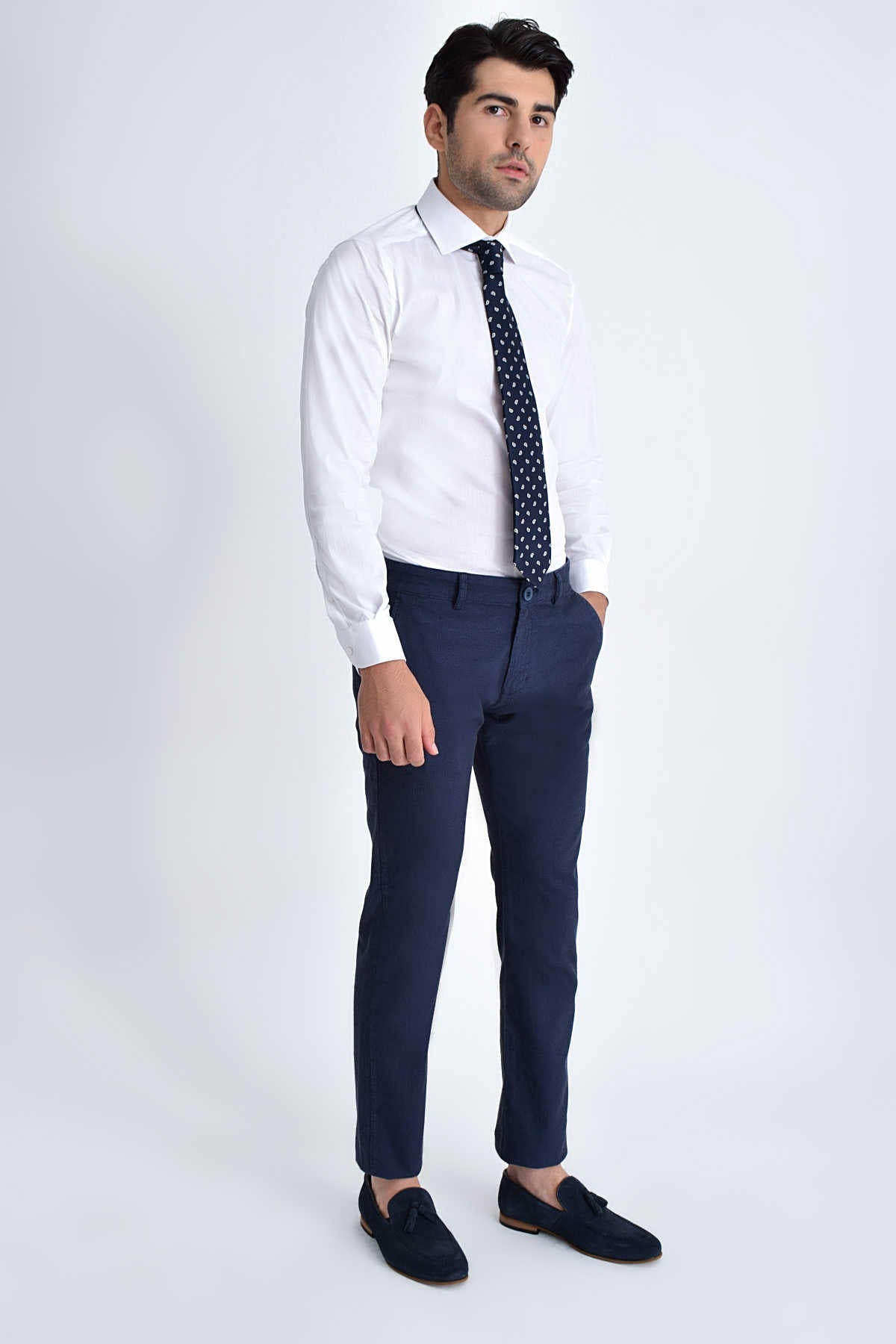 A man wearing a crisp white dress shirt, navy blue tailored trousers with a subtle sheen and matching dark loafers.