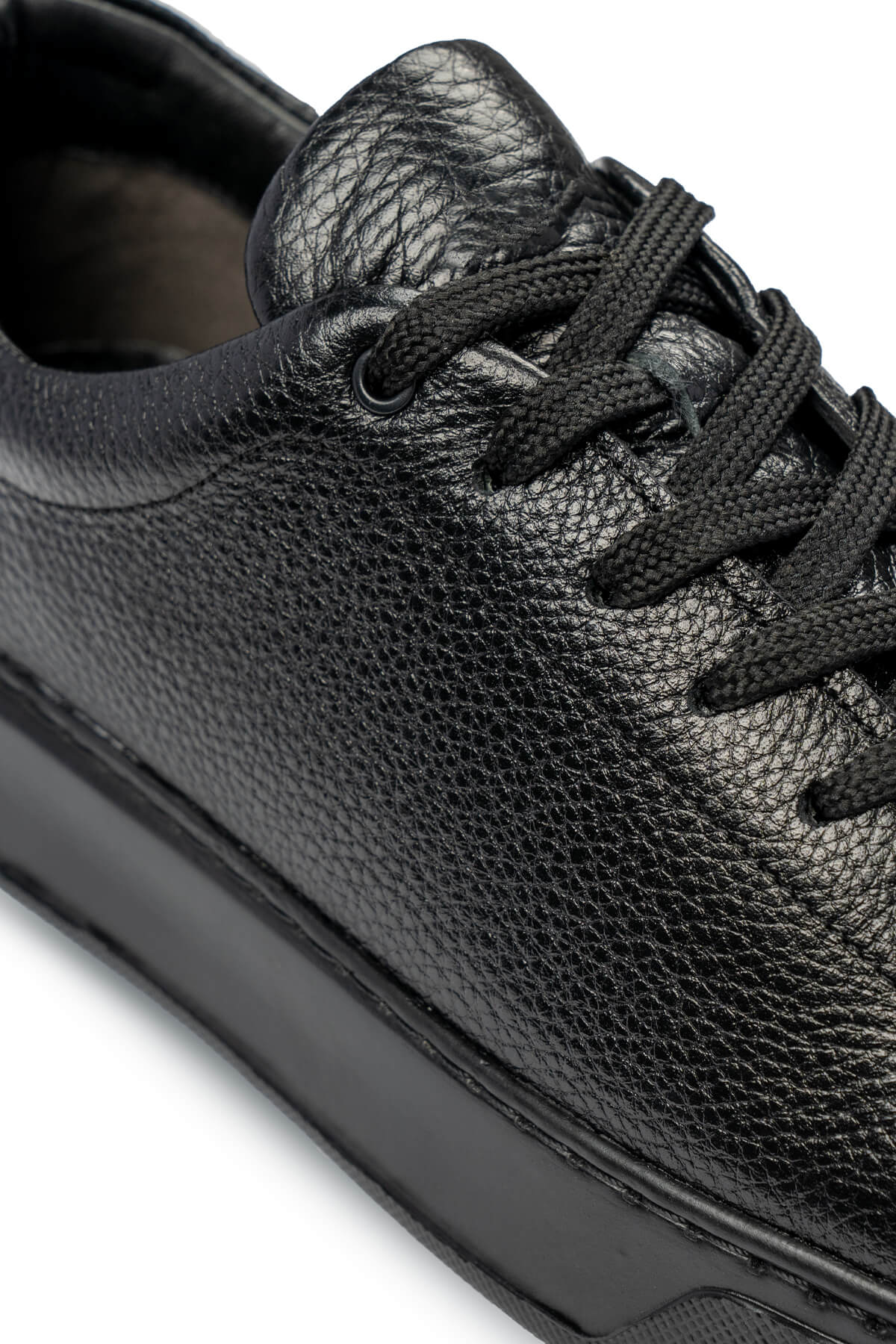 Black pebbled leather low-top sneaker with black laces and a matte rubber sole.