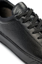 Black pebbled leather low-top sneaker with black laces and a matte rubber sole.