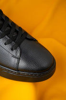 Black leather sneaker with textured surface and matching laces.