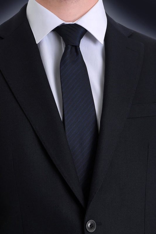A sleek black tie with a subtle textured pattern, worn neatly against a crisp white dress shirt and dark suit.