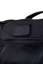Black sayki brand duffel bag with a textured fabric body and stitched leather-like patch.